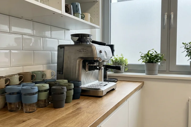 Stilvolle Mehrwegbecher und Keramiktassen neben einer professionellen Kaffeemaschine